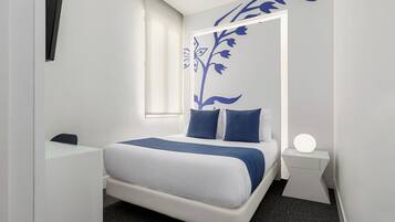 Habitació d'hotel moderna amb un llit, una escriptori i una tauleta de nit amb una làmpada.