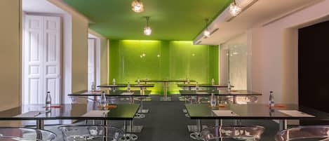Een vergaderzaal met een groene accentmuur, transparante glazen stoelen en een lange tafel met waterflesjes.