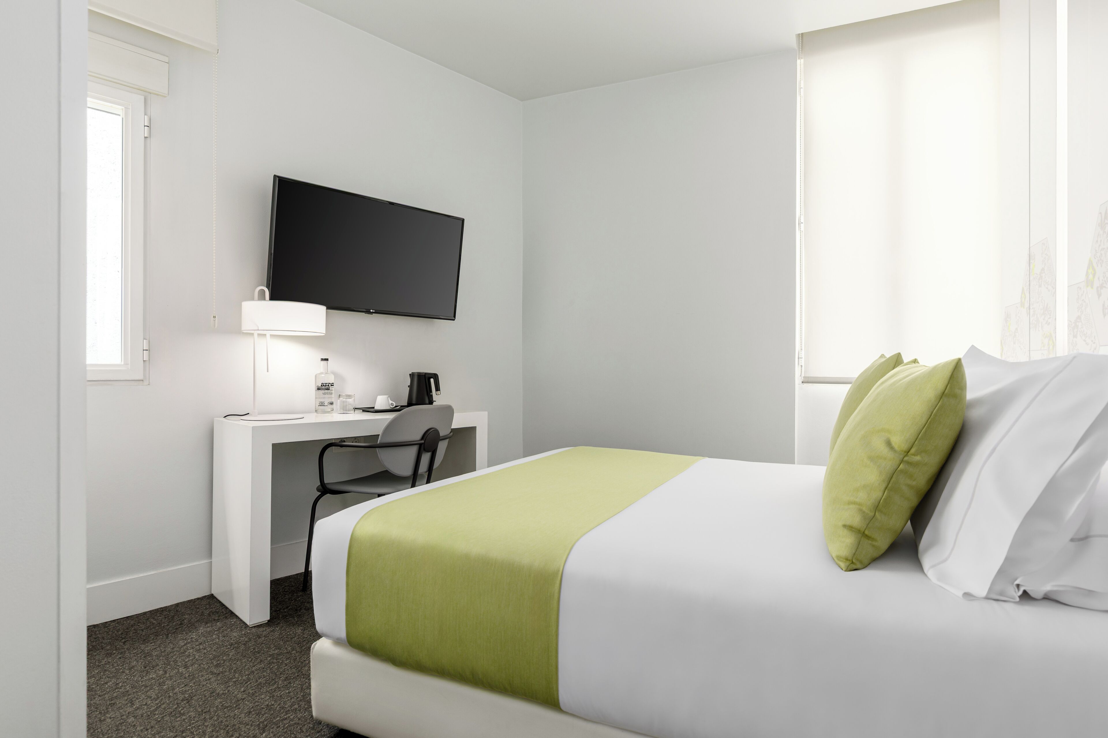 Een hotelkamer met een bed, een bureau, een stoel, een televisie en een raam met gordijnen.