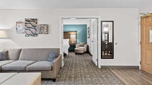 Et hotelværelse med sofa, skammel og en gang der fører til et spiseområde.