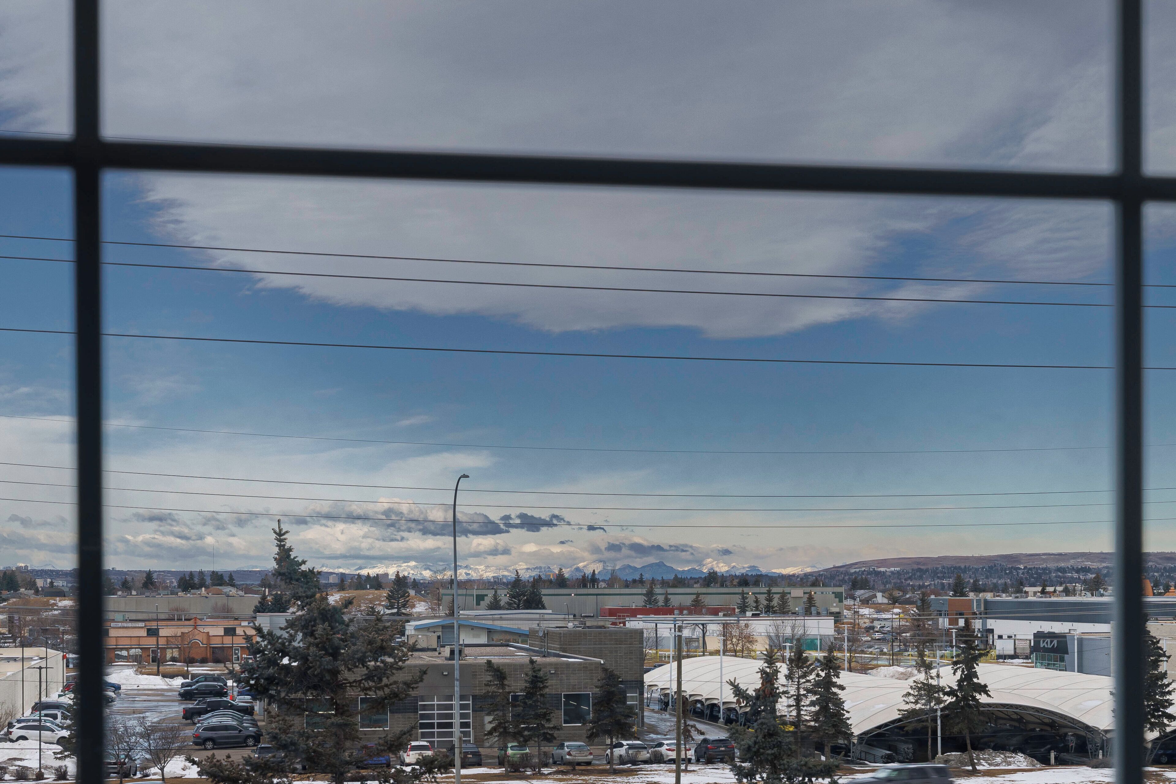 A view through a window of a parking lot with buildings, trees, and a clear sky.