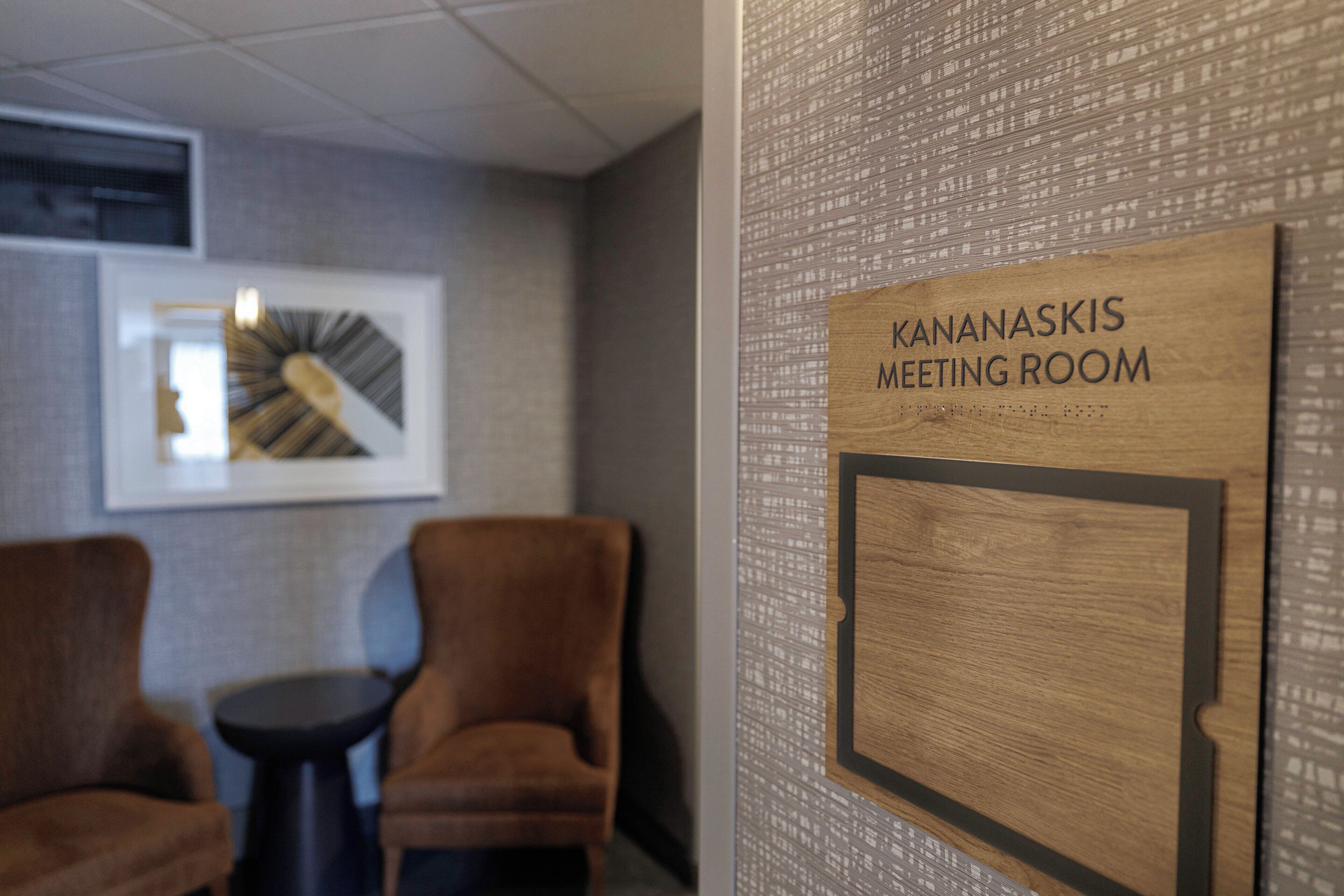 A meeting room with a sign, two chairs, a small table, and a framed picture on the wall.