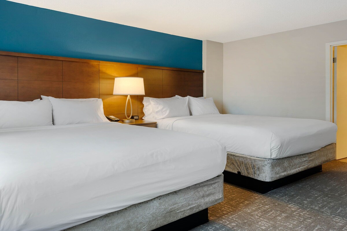 A hotel room with two beds, a nightstand with a lamp, and a blue accent wall.