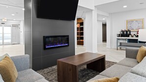 En moderne lobby med et fladskærms-tv, pejs, siddeområde med sofaer og en bar med flasker.