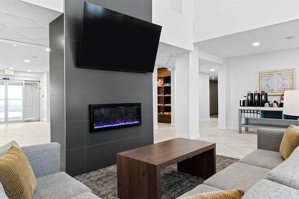 A modern lobby with a flat-screen TV, a fireplace, a seating area with sofas, and a bar area with bottles. - Staybridge Suites Calgary Airport by IHG (Calgary)