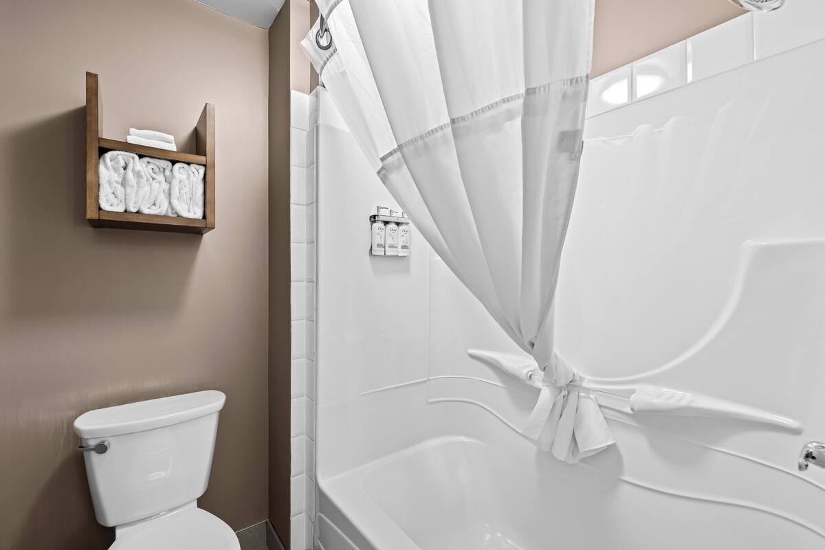 A bathroom with a toilet, a shower with a curtain, and a shelf with towels.