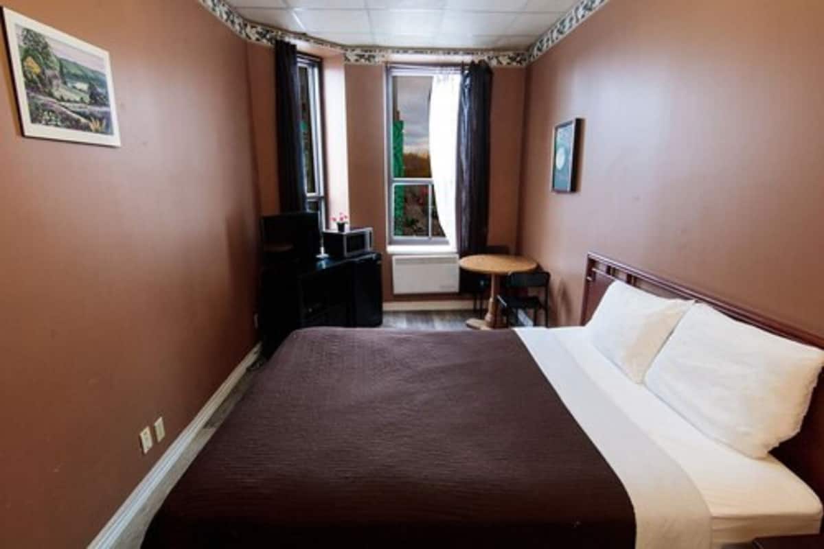 A bedroom with a large bed, a small table, a chair, a TV, and a window with curtains.
