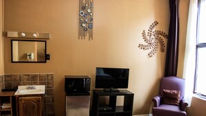 Un espacio habitable compacto con kitchenette, un televisor de pantalla plana, un elemento decorativo en la pared y una ventana con cortinas.