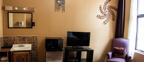 A compact living space with a kitchenette, a flat-screen TV, a decorative wall piece, and a window with curtains.