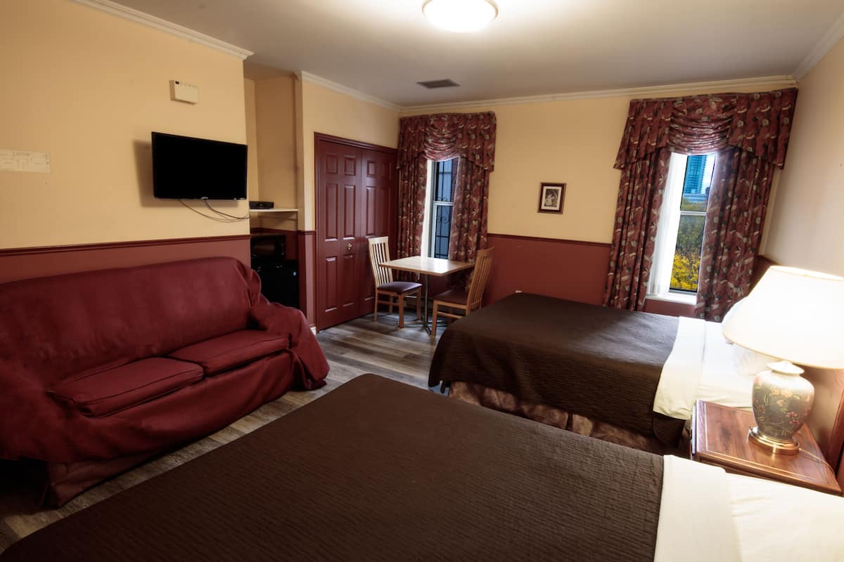 A hotel room with a sofa, two single beds, a table, a chair, a TV, and a window with curtains.