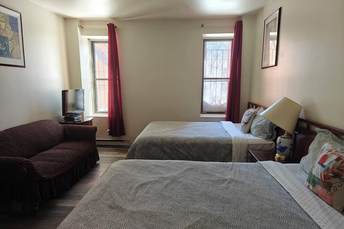 A hotel room with two beds, a sofa, a TV, and a lamp.