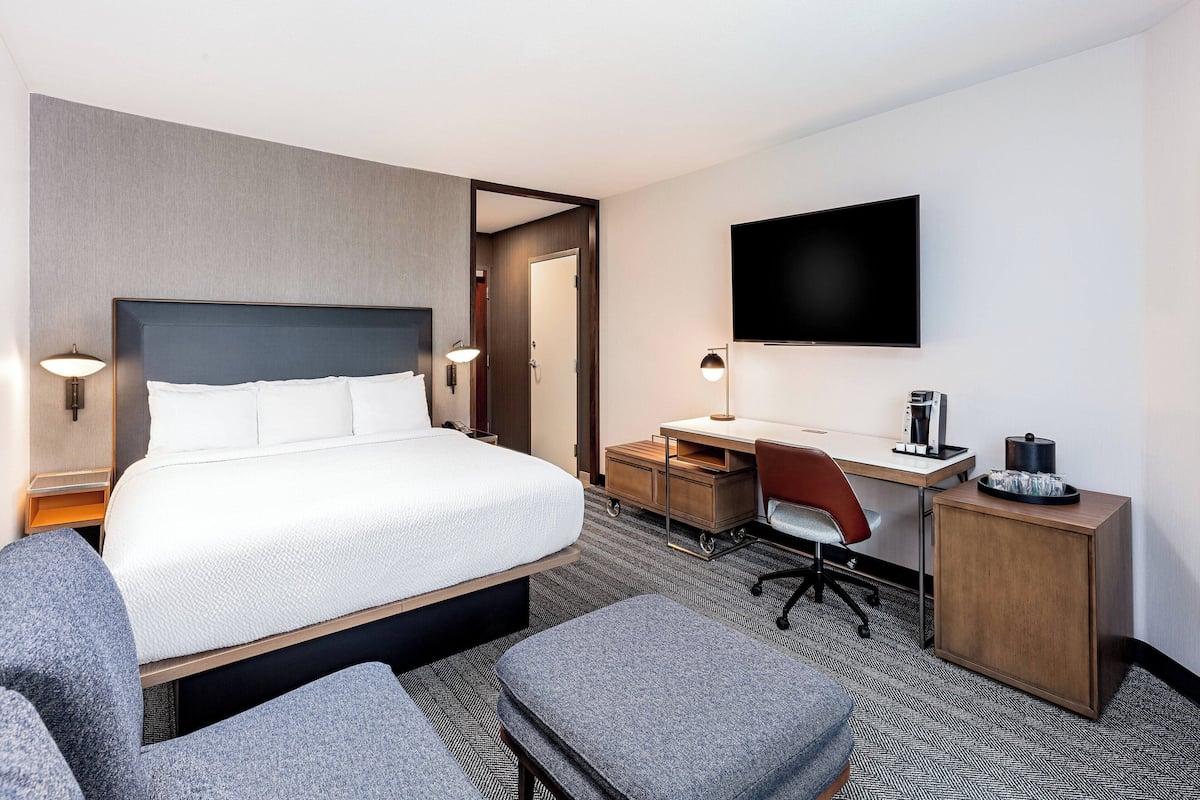 A hotel room with a large bed, a desk, a chair, a TV, and a small cabinet.