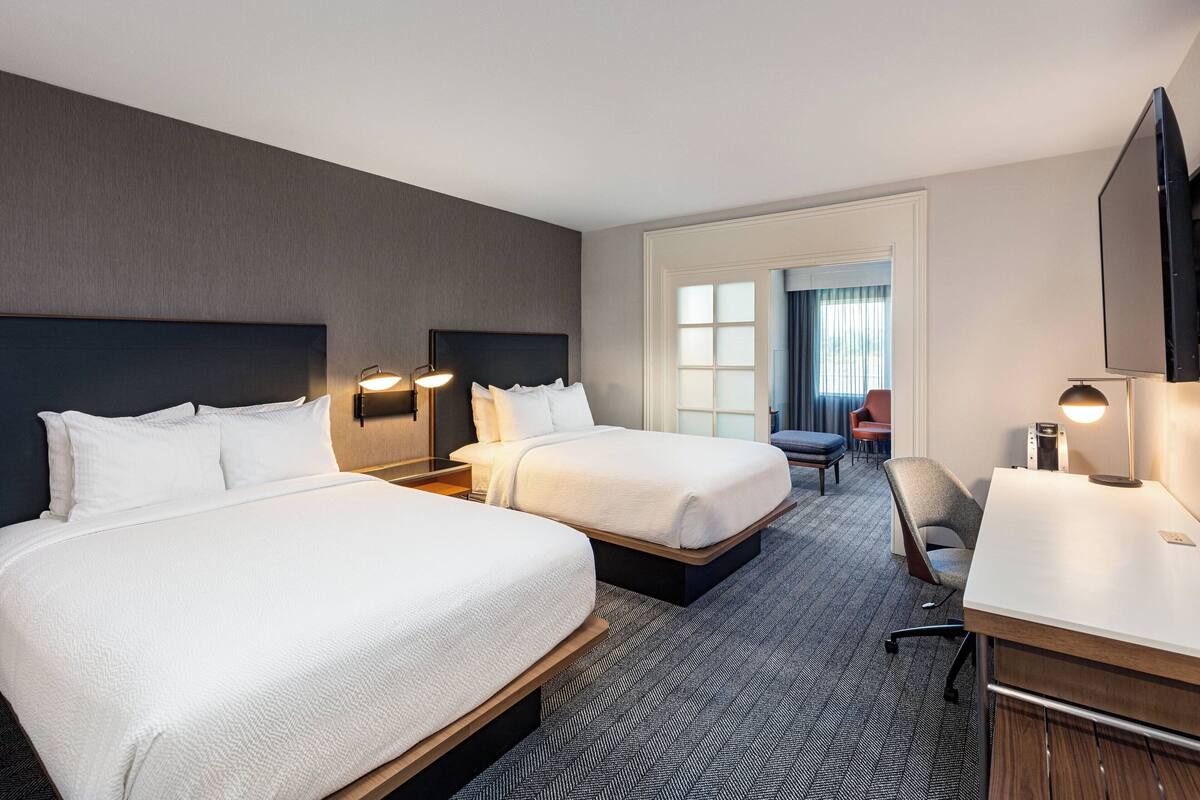 Ett hotellrum med två sängar, ett skrivbord, en stol och en tv.