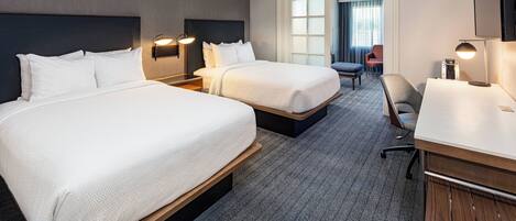 A hotel room with two beds, a desk, a chair, and a TV.