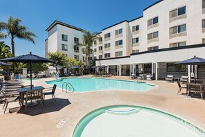 Un espace piscine d’hôtel avec des chaises longues, des parasols et une piscine à l’eau d’un bleu limpide.