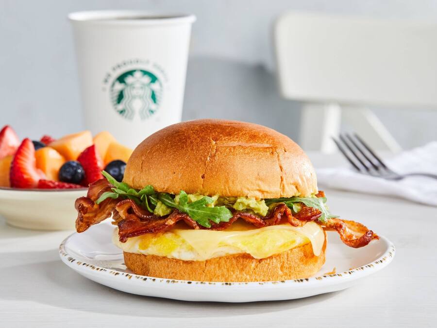 A breakfast sandwich on a plate with a Starbucks cup in the background.