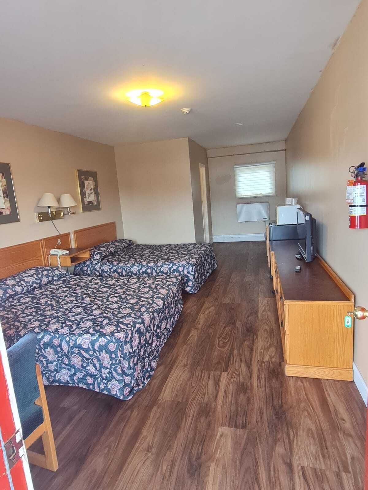A room with a bed, a desk, a chair, a fire extinguisher, and a window.