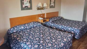 A room with two beds, a wooden headboard, a nightstand with a lamp, and framed pictures on the wall.
