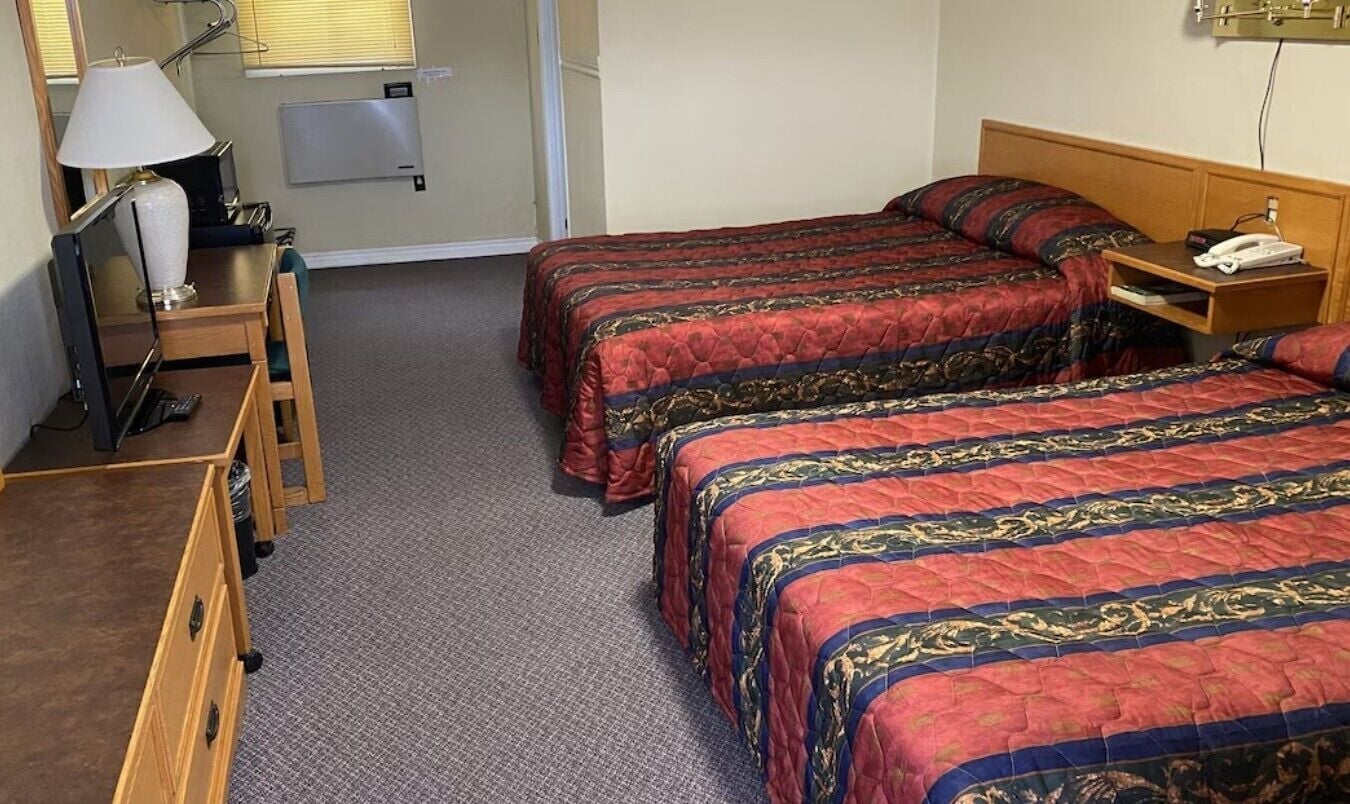 A hotel room with two beds, a desk with a lamp, a chair, and a telephone.