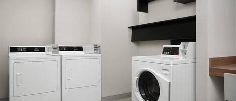 A laundry room with two front-loading washers and a dryer, a coffee maker, and black shelving units.