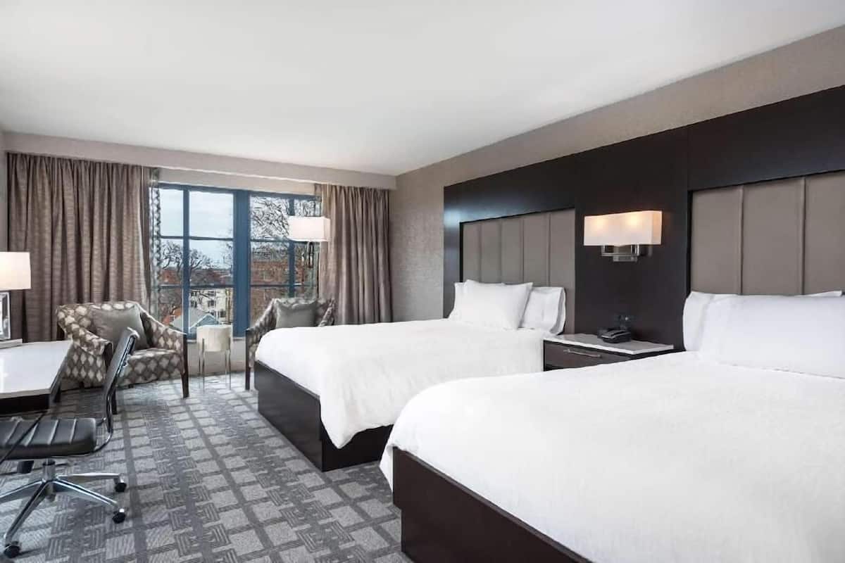 Ein Hotelzimmer mit zwei Betten, einem Schreibtisch, einem Stuhl und Blick auf die Stadt.
