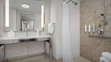 Un baño moderno con un espejo grande, un lavamanos, ducha con cabezal de ducha manual y artículos de tocador sobre la encimera.