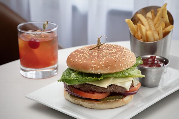 Una hamburguesa con papas fritas y una bebida en un plato blanco.