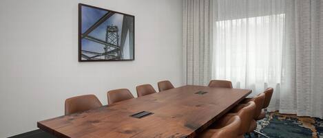 A conference room with a large wooden table, leather chairs, a framed picture on the wall, and a large window with sheer curtains.