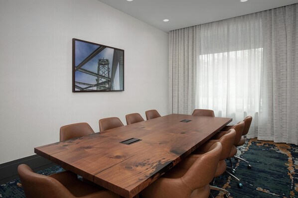 Une salle de conférence dotée d’une grande table en bois, de fauteuils en cuir, d’un tableau encadré au mur et d’une grande fenêtre ornée de rideaux légers.