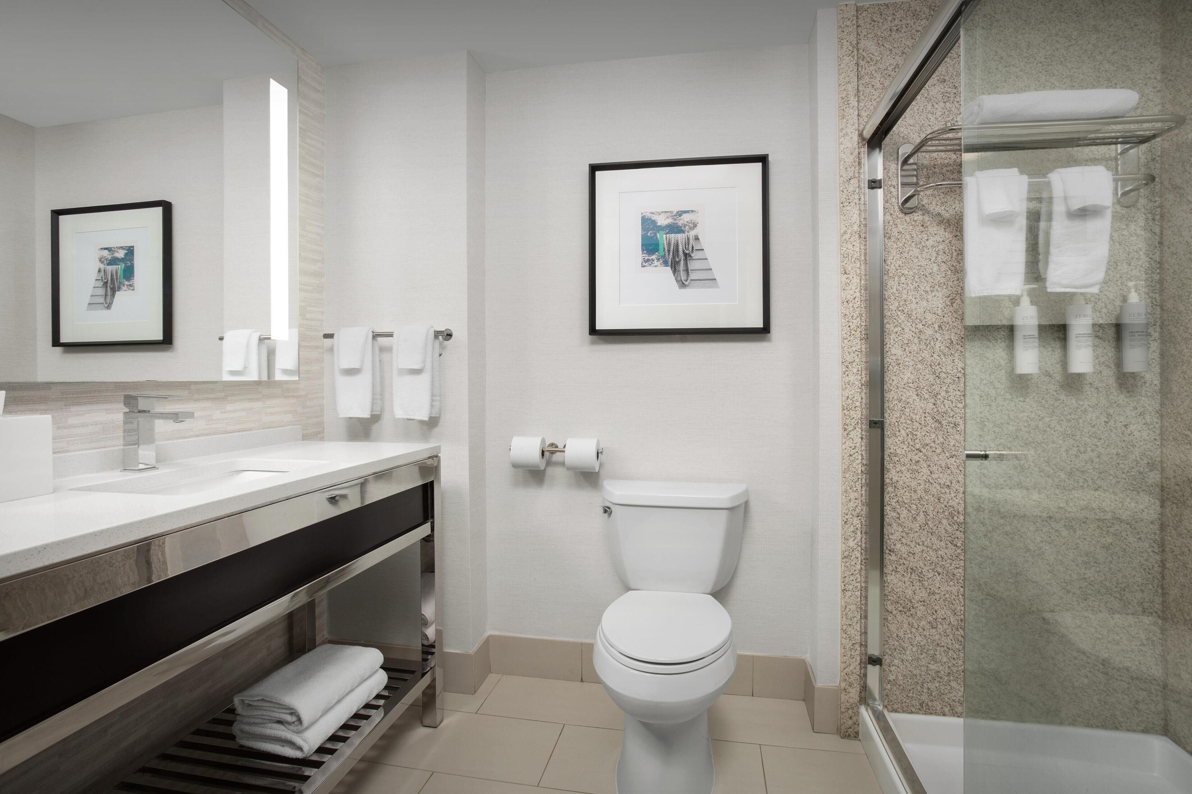 Une salle de bain moderne avec des toilettes, un lavabo et un espace douche. Des tableaux encadrés ornent le mur et des serviettes sont disposées sur le porte-serviettes de la douche.
