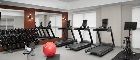 A gym with treadmills, dumbbells, a red exercise ball, and a stationary bike.