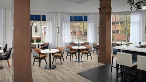 A modern dining area with round tables and chairs, large windows with curtains, and a view of the outside. - Hilton Garden Inn Portsmouth Downtown (Portsmouth)