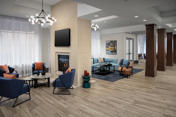 A spacious hotel lobby with a fireplace, modern seating, and a large flat-screen TV mounted on the wall.