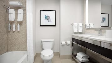 A modern bathroom with a toilet, bathtub, and a vanity with a mirror. There are towels and toiletries on the wall.