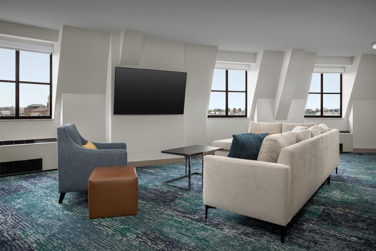 Ein modernes Hotelzimmer mit einem großen Flachbildfernseher, einem Sofa, einem Sessel und einem kleinen Tisch.