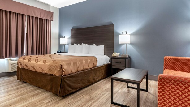 Ein Hotelzimmer mit einem großen Bett, Nachttischlampen, einem kleinen Tisch und einem Sessel.