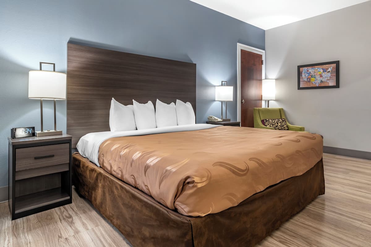 A hotel room with a large bed, two bedside tables with lamps, a green chair, and a wall map.