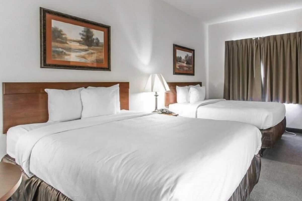 A hotel room with two beds, a wooden headboard, a lamp, and two framed pictures on the wall.
