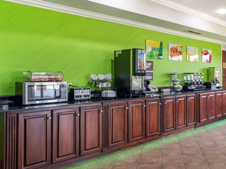 Una larga encimera con una cafetera, microondas y diferentes recipientes de comida.