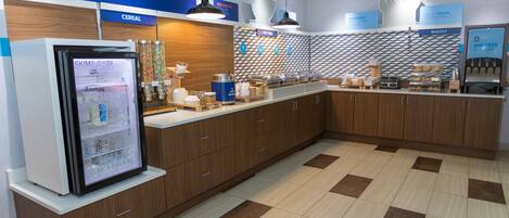 Un espace moderne dédié au petit-déjeuner, équipé d’un présentoir réfrigéré, d’un rayon de céréales et d’une boulangerie.