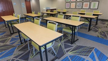Un salón de conferencias con varias mesas y sillas, piso alfombrado y cuadros en la pared.