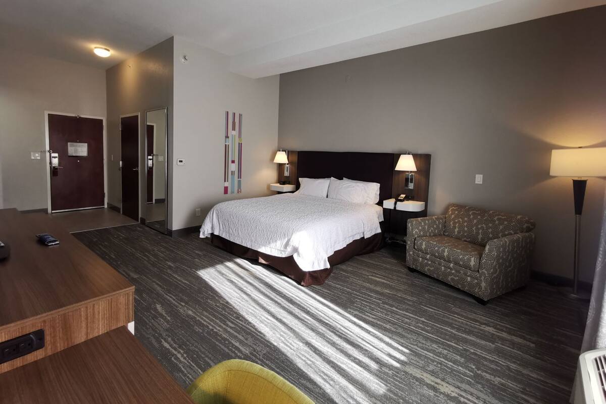 A hotel room with a bed, bedside tables, a desk, a chair, and a lamp.