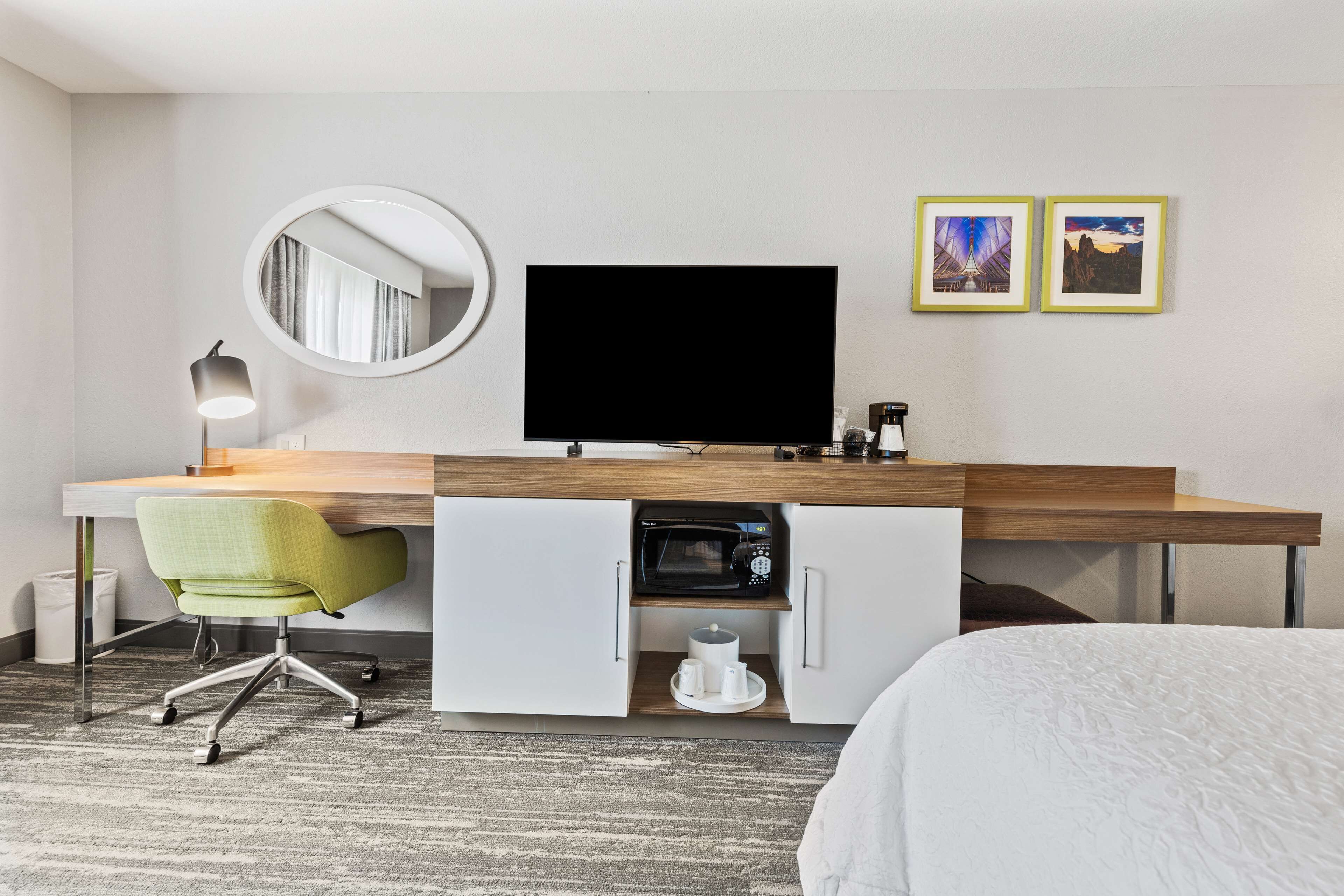 Une chambre d’hôtel équipée d’un lit, d’un bureau avec un téléviseur à écran plat, d’un fauteuil vert, d’un four à micro-ondes et d’une machine à café.