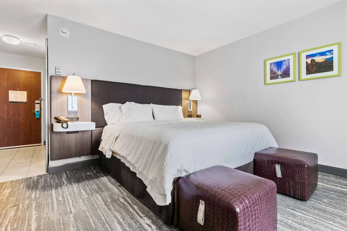 A hotel room with a large bed, bedside lamps, a nightstand, a small table, and two framed pictures on the wall.