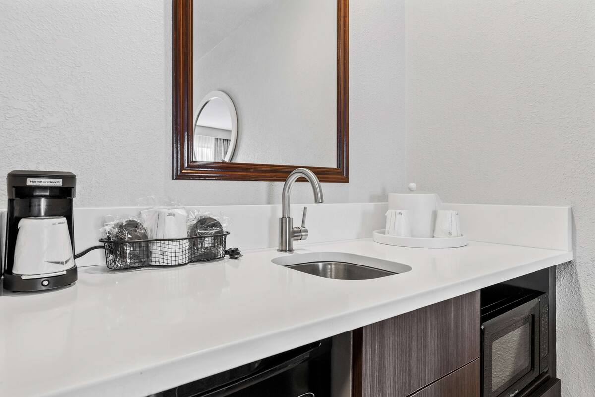 A hotel bathroom with a white sink, a coffee maker, a mirror, and a microwave.