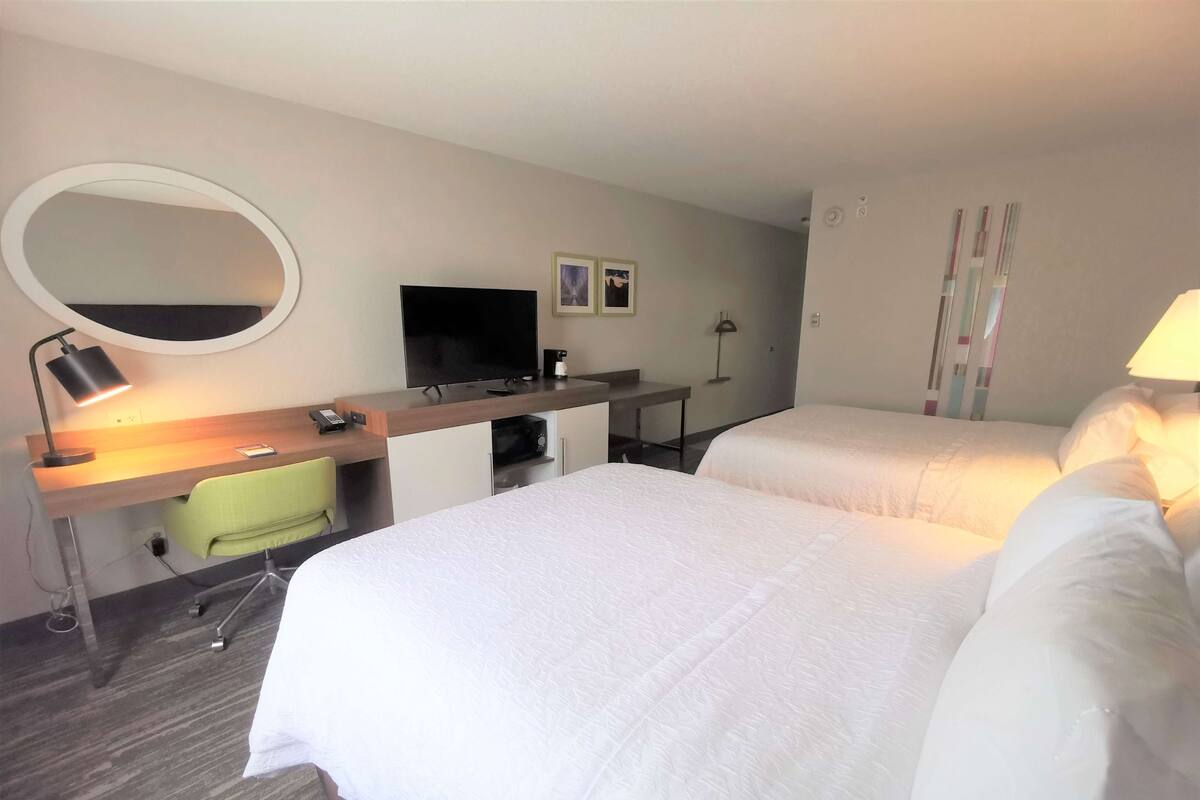 A hotel room with two beds, a desk with a computer, a TV, and a mirror.