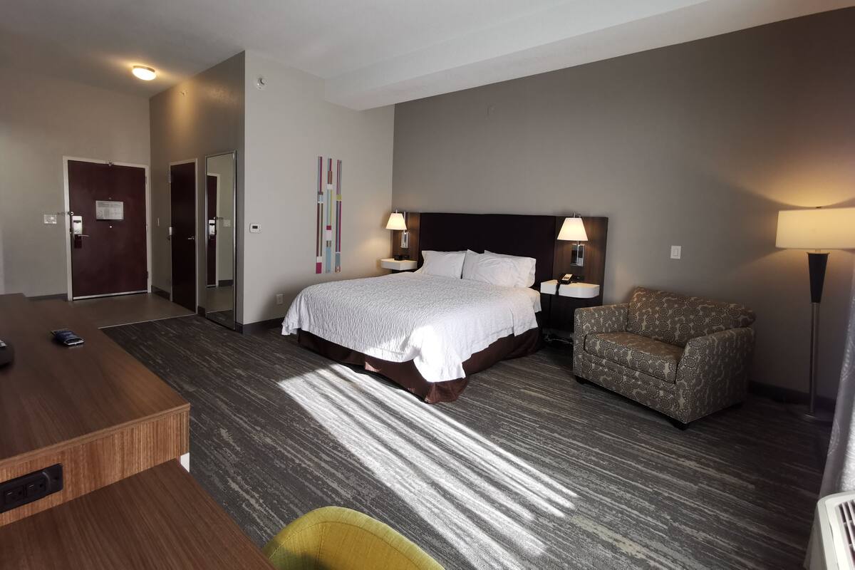 A hotel room with a bed, bedside tables, a desk, a chair, and a large mirror.