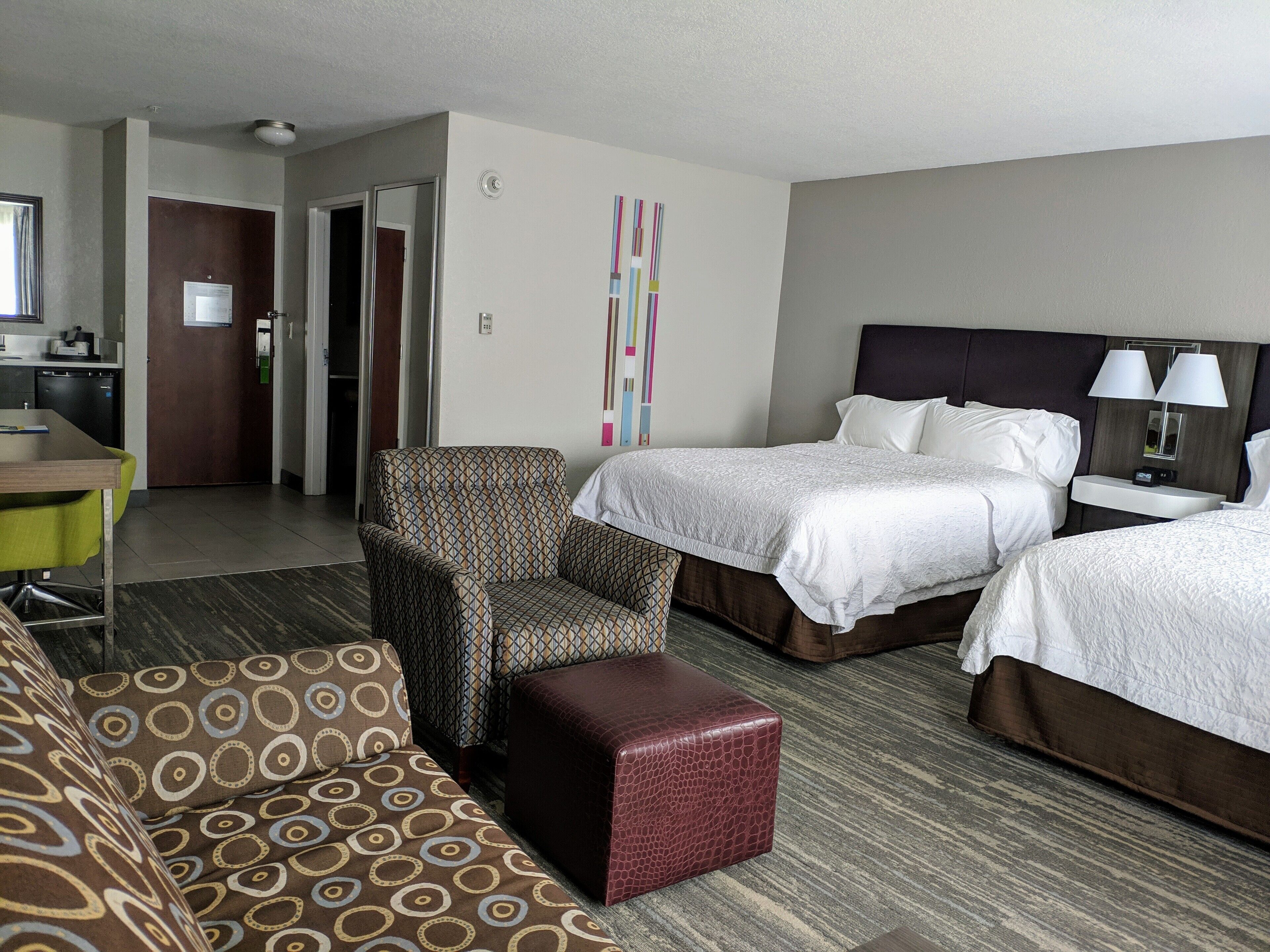 A hotel room with two beds, a sofa, a small table, and a kitchenette.