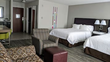 A hotel room with two beds, a sofa, a small table, and a kitchenette.