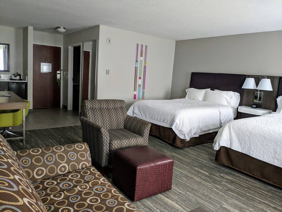 A hotel room with two beds, a sofa, a small table, and a kitchenette.